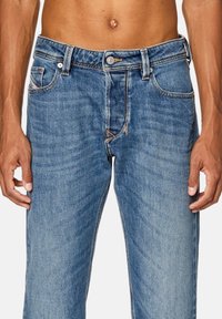 Ljust blå denimjeans med rak passform, framfickor och stickade detaljer. Har en dragkedja fram och en knäppning i midjan.