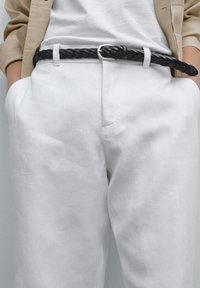 Schwarzer geflochtener Ledergürtel mit silberner Metallschnalle, getragen zu weißen Leinenhosen und einem hellen Oberteil. Minimalistisches Design und Textur.