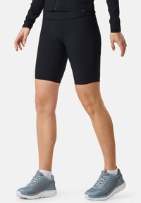 Shorts da ciclismo neri a coste con un design a vita alta, abbinati a scarpe sportive grigie con una tomaia testurizzata e suole bianche.