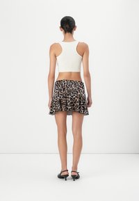 Weißes Crop-Top, ausgestellter Leopardenmuster-Rock, schwarze Absätze. Der Rock zeichnet sich durch ein lebhaftes Tiermuster und eine leichte, fließende Textur aus.