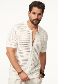 Weißer, kurzärmeliger, knöpfbarer Pullover mit einem gestrickten Netzdesign. Verfügt über einen klassischen Kragen und eine taillierte Silhouette mit gerippten Bündchen.