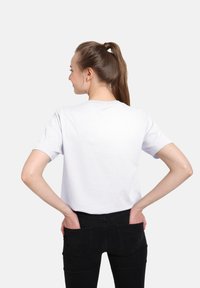 Hvid bomulds t-shirt med korte ærmer, rund halsudskæring, afslappet pasform, set fra ryggen, parret med sorte bukser. Ingen synlige logoer eller mønstre.