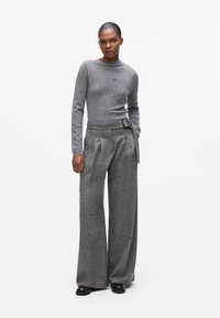 Grauer Wollpullover mit Bootsausschnitt, kombiniert mit grauen weit geschnittenen Hosen mit einem taillierten Bund und gefaltetem Vorderteil. Strukturiertes Material.