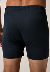 Boxer shorts blu scuro realizzati in un tessuto liscio e stretch, con una cintura elastica, presentano un design aderente e senza motivi visibili.