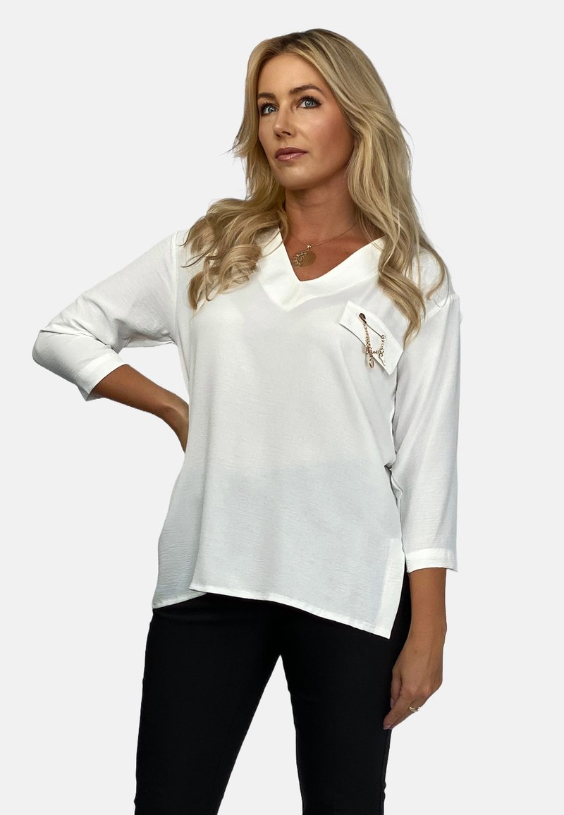 Biała bluzka z dekoltem w serek i rękawami do trzech ćwiartek, z kieszonką na piersi i akcentem w postaci łańcuszka. Wykonana z lekkiego, strukturalnego materiału.