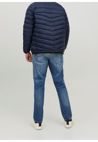 Marineblauer Pufferjacke mit Zickzacksteppung, kombiniert mit hellblauen Jeans und weißen Sneakers mit schwarzen Akzenten.