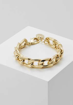 Bracelet chaîne épaisse en or avec maillons ovales et fermoir mousqueton, reposant sur un cube blanc sur un fond gris clair.