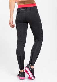Czarne legginsy sportowe z wysokim różowym pasem w talii, z zamkiem błyskawicznym na tylnej kieszeni i zamkami po bokach na kostkach. Na nogach znajdują się buty Reebok.