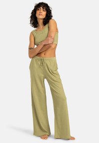 Ensemble de vêtements de détente vert clair comprenant un top sans manches et court ainsi que des pantalons larges. Texture douce, coupe décontractée et taille à cordon.
