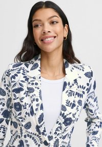 Blazer floreale con sfondo bianco e motivi botanici blu navy, rever a punta e chiusura con un solo bottone.