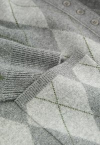Grå sweater med argyle-mønster i grønne og hvide diamantformer, ribbede ærmer og brune knapper på kraven.
