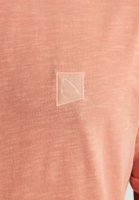 T-shirt color pesca realizzato in tessuto testurizzato con un patch cucito che presenta un design triangolare minimalista.