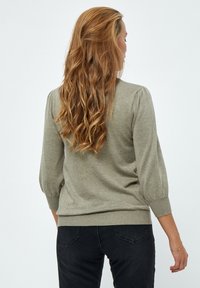 Olivgrön stickad tröja med puffärm och ribbad nederkant. Mjuk textur och figurnära passform, bärs med svarta jeans.