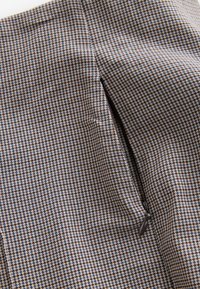 Tissu pied-de-poule beige et bleu avec une poche zippée, présentant une texture lisse et un design structuré.