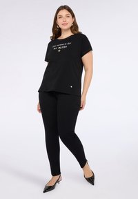 Camiseta de algodón negra de manga corta, con texto blanco y un gráfico de sol, combinada con pantalones negros ajustados y zapatos de punta.
