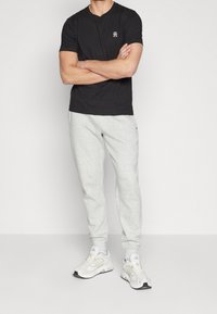 Camiseta negra de manga corta con un pequeño logo, combinada con pantalones de chándal gris claro y zapatillas deportivas blancas. Tejido texturizado, corte relajado.