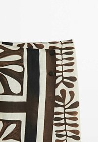 Linnen rok met een mix van donkerbruin en roomkleuren, versierd met botanische prints, twee zwarte knopen en een lineair patroon.