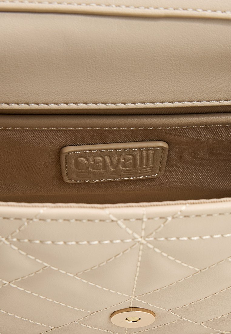 Interior de bolso de cuero beige, con textura acolchada, una etiqueta con el logo y forro marrón claro. Cierre de botón con detalle en dorado.