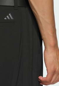 Svarta sportshorts i strukturerad tyg, med en sidoficka och en grå Adidas-logotyp på vänster sida nära midjebandet.