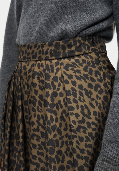 Κοντινή λήψη της μέσης και των πιέτων φούστας με λεοπάρ μοτίβο, σε συνδυασμό με γκρι πλεκτό πουλόβερ με μακριά μανίκια.