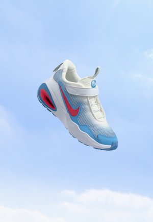 Une basket Nike blanche et bleue, ornée d’un Swoosh rouge, flotte sur fond de ciel bleu dégagé.