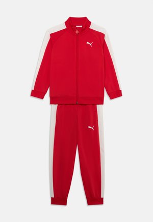 Rdeč trenirko, ki vsebuje jakno z zadrgo in belimi ramenskimi poudarki ter ujemajoče se rdeče hlače. Narejena iz gladkega, lahkega materiala. Prisutni logotip Puma.