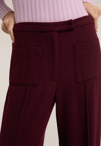 Bordowe spodnie o szerokich nogawkach wykonane z miękkiego materiału, z dwoma przednimi kieszeniami i gładkim detalem w pasie, o luźnym kroju.