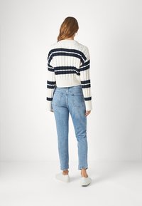 Suéter crema recortado con rayas azul marino, textura acanalada. Jeans ajustados de mezclilla azul claro. Zapatillas blancas con acentos sutiles sobre un fondo liso.