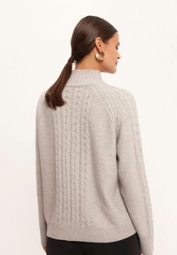 Jasnoszara dzianinowa sweter z wysokim kołnierzem i wzorem w warkocze na plecach. Projekt zawiera ściągacze przy mankietach i dolnym wykończeniu.