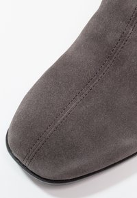 Gros plan sur l'avant d'une chaussure en daim gris avec une couture centrale visible et un bord de semelle noir.