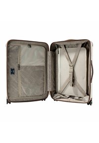 Walizka o twardej skorupie w jasnobeżowym kolorze, wyposażona w wzorzyste wnętrze, kieszeń z siatki na zamek oraz regulowane paski zapewniające bezpieczne pakowanie.