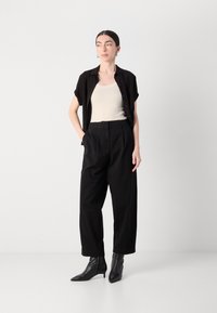 Svart kortermet skjorte, beige tanktop, høyt liv svarte bukser, og spisse svarte ankelstøvler. Enkelt, moderne design med rene linjer.