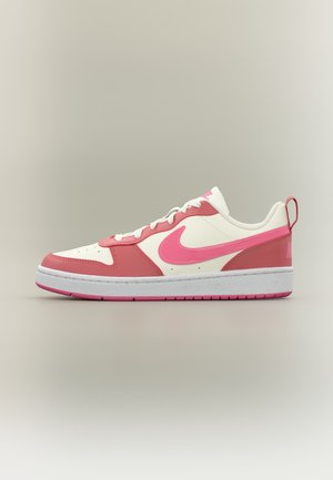 Baskets basses Nike blanches et roses avec lacets blancs, logo swoosh rose et semelle épaisse blanche avec crampons roses.