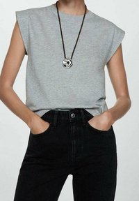 T-shirt gris à manches courtes avec une coupe décontractée, associé à un jean noir taille haute. Un collier avec un pendentif rond en métal ajoute une touche de détail.