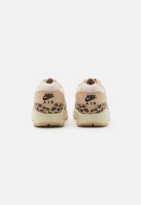 Nike Air sporta apavi ar smilšu krāsas augšdaļu, struktūrētu zamšādu un tīklu, ar leoparda rakstu akcentu uz papēža un krēmkrāsas zoli.