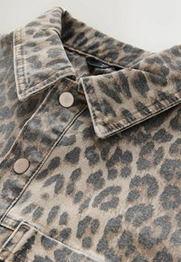 Leopardmuster-Hemd aus Denim, mit spitzem Kragen, Knopfverschluss und einer Farbkombination aus Beige und Schwarz sowie einer strukturierten Oberfläche.