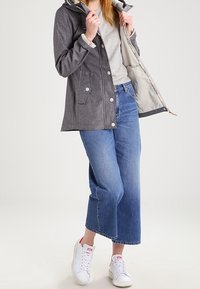 Gray hooded jacket with snap buttons and pockets, worn over a light gray shirt. Paired with wide-leg blue jeans and white sneakers.