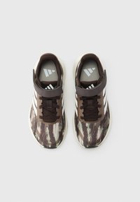Αθλητικά παπούτσια με μοτίβο παραλλαγής σε καφέ και πράσινες αποχρώσεις, λευκό λογότυπο με τρεις ρίγες και μαλακή σόλα. Περιλαμβάνει ρυθμιζόμενο ιμάντα βέλκρο.