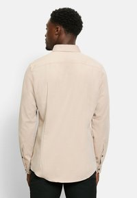 Beige Langarmhemd mit strukturiertem Muster, Knopfmanschetten und klassischem Kragen. Verfügt über einen abgerundeten Saum und ein Rückenpasse-Design.