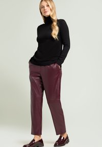 Zwarte coltrui gecombineerd met bordeauxrode leren broek. Soepele textuur en een nauwsluitende pasvorm, aangevuld met glanzende zwarte loafers.