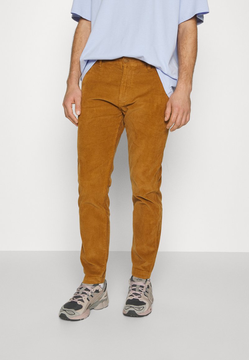 Un pantalon en velours côtelé marron à coupe slim, avec une surface texturée et un design classique à cinq poches, assorti de baskets texturées.