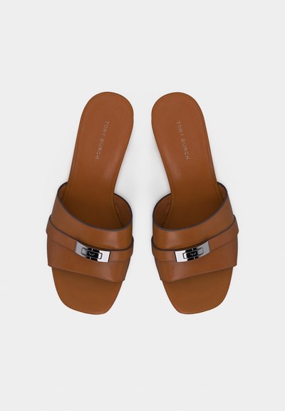 Καφέ δερμάτινα σανδάλια slide με ασημένια αγκράφα και τετράγωνη μύτη, επίπεδη σόλα, με το λογότυπο Tory Burch στο εσωτερικό της σόλας.