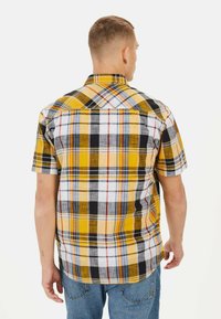 Korte mouwen geruite shirt in geel, zwart en wit; heeft een ruitpatroon met verschillende kleurvlakken en een puntige kraag.