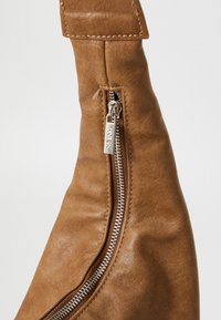 Braune Lederhandtasche mit strukturiertem Oberflächenmaterial, ausgestattet mit einem silbernen Reißverschluss und einer stabilen Riemenbefestigung. Minimalistisches Design.