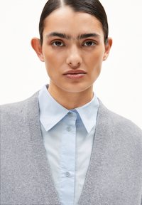 Grauer Cardigan über einem hellblauen Hemd. Der Cardigan hat eine weiche Textur und ein V-Ausschnitt-Design. Das Hemd hat einen klassischen Kragen und Knöpfe.