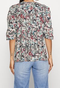 Blusa con motivo floreale, con maniche a sbuffo corte, sfondo beige chiaro e intricate fantasie paisley nei toni del rosso, blu e verde.