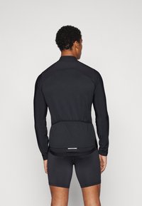 Black long-sleeve sports jersey with a fitted design, textured shoulder panels, and a waistline hem, paired with black shorts.