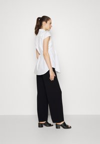 White short-sleeve shirt with gathered back and rounded hem, paired with black wide-leg trousers and black block-heeled sandals.