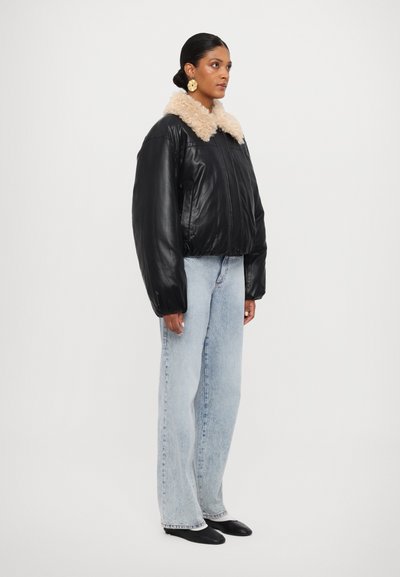 Veste bomber en cuir noir avec un col en fausse fourrure beige, fermeture éclair à l'avant et manches volumineuses, associée à un jean droit bleu clair.