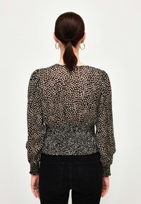 Blusa a pois neri e crema con maniche lunghe, vita arricciata e tessuto trasparente. Indossata con jeans neri, vista dal retro.